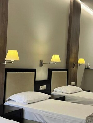 Habitación de hotel con dos camas individuales, cada una con cabecera y mesita de noche. Hay tres lámparas fijadas a la pared que proporcionan luz.