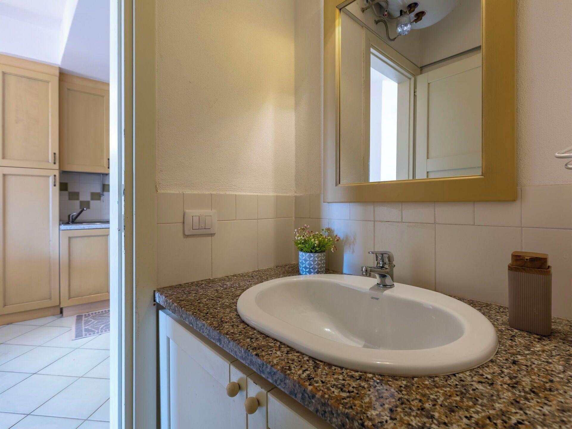 A bathroom with a granite countertop, a white sink, a mirror, and a potted plant.