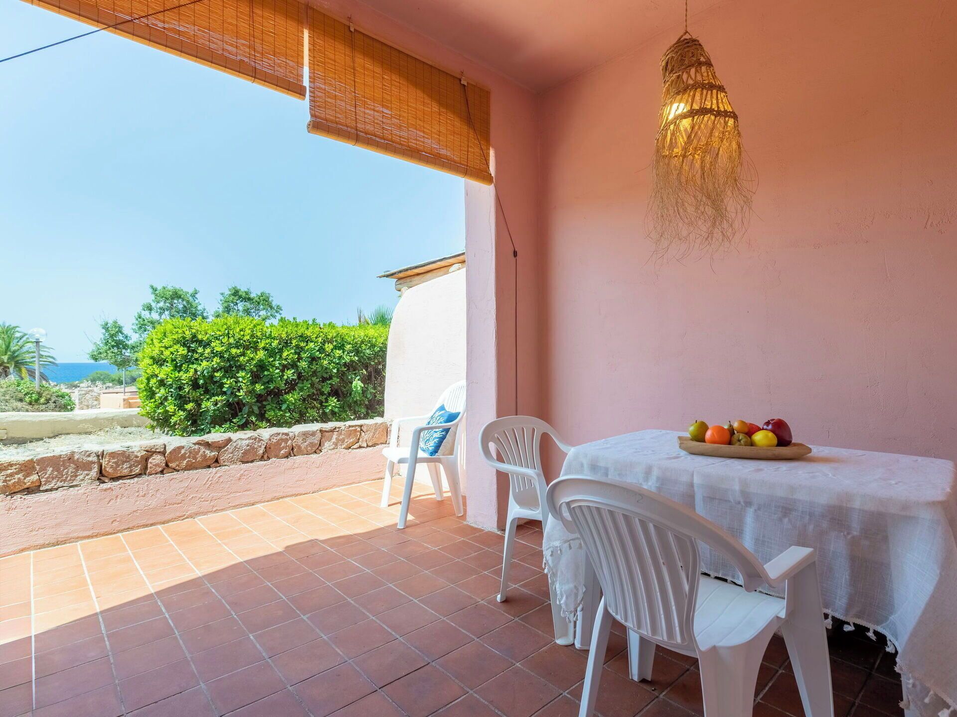 Une terrasse avec une table et des chaises, un luminaire suspendu et une vue sur la verdure et la mer.