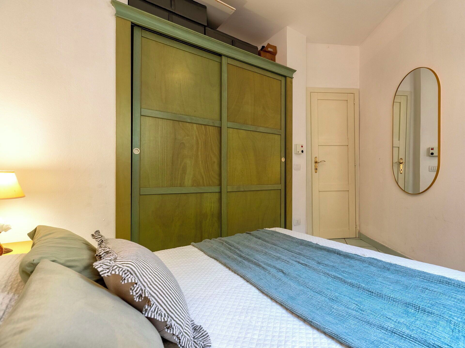 Un dormitorio con cama, almohadas, una colcha, un armario, una puerta y un espejo.