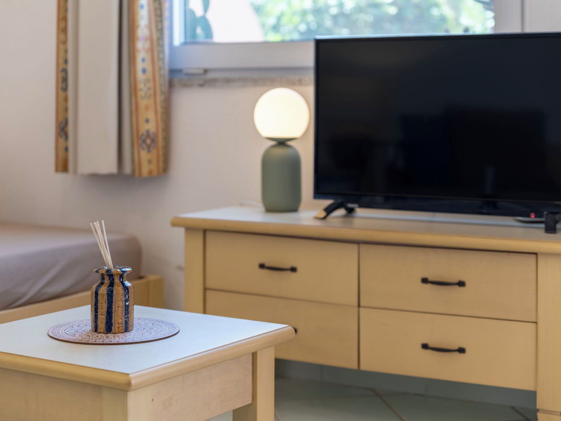 A room with a bed, a TV on a stand, a lamp, and a small table with a candle holder.