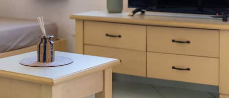 A room with a bed, a TV on a stand, a lamp, and a small table with a candle holder.
