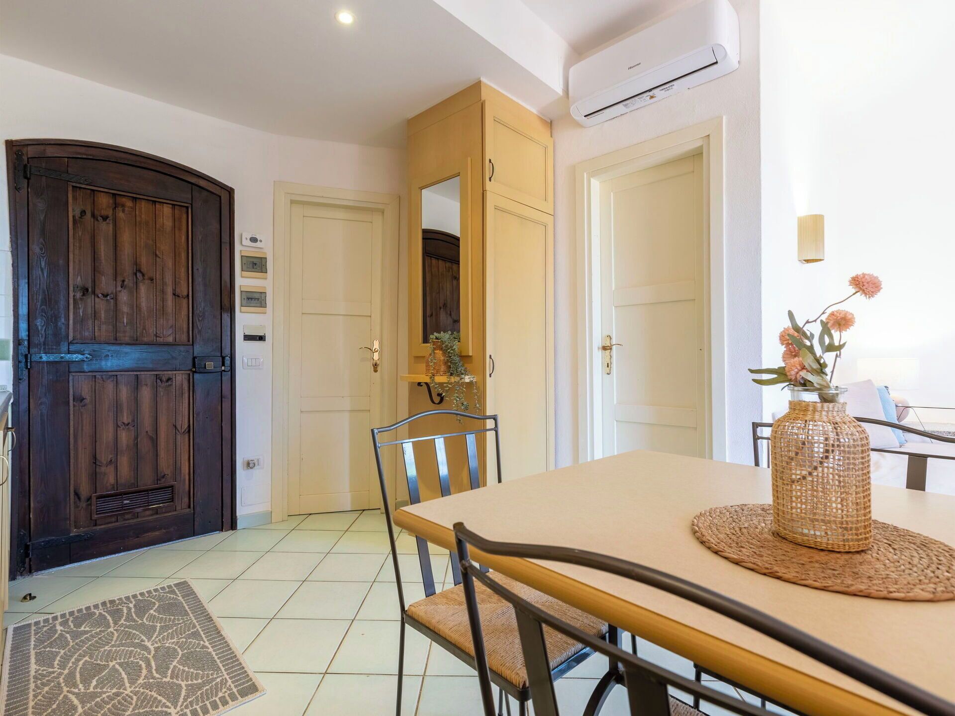A dining area with a table, chairs, a vase with flowers, and a large wooden door.