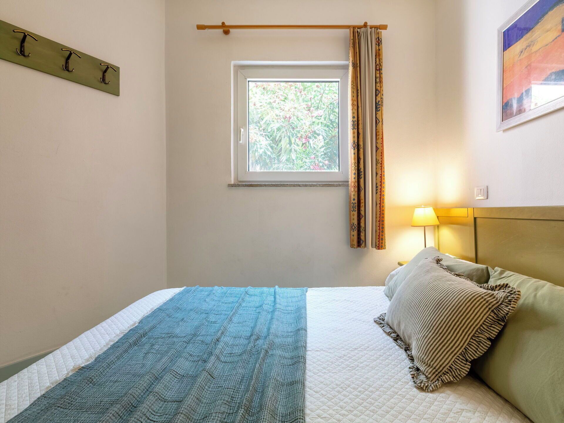 A bedroom with a bed, a window, a bedside lamp, and a wall-mounted light switch.