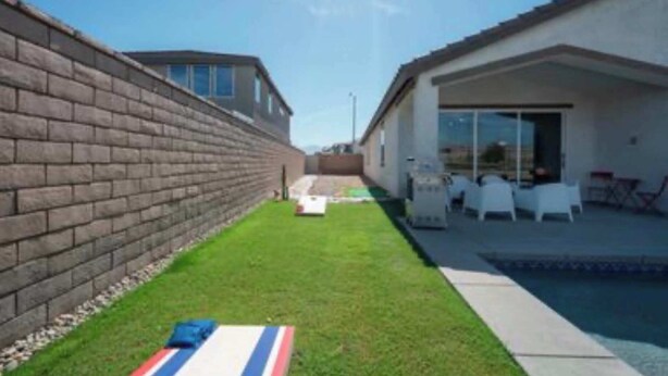 A backyard with a brick wall, a grassy area, and a poolside area with chairs. - Saltwater Pool, Spa & Casita  Terra Lago (Indio)