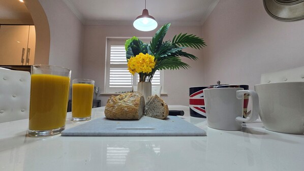 Een ontbijttafel met een brood, twee glazen jus d'orange, een mok en een decoratieve plant.