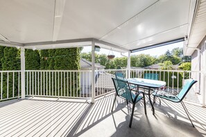 A covered outdoor area with a table and chairs, surrounded by a white railing, and a green hedge in the background. - Spacious 5BR Family Home in North Delta, BC (Delta)