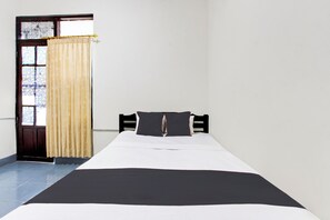 A single bed with a black and white bedspread, a wooden headboard, and a window with a curtain. - OYO 95377 Roemah Lawas (Yogyakarta)