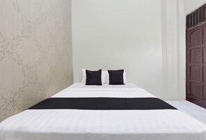 Una cama bien hecha con ropa blanca y dos almohadas negras, una manta oscura y un estampado floral en la pared.