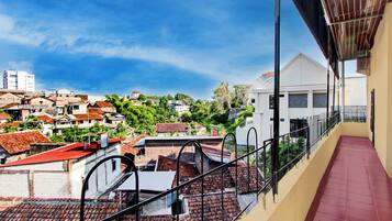 A balcony with a red-tiled floor and a view of a residential area with houses and greenery.