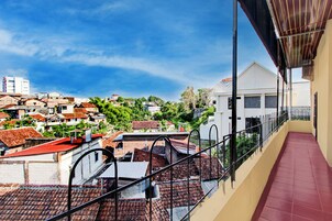 Un balcón con piso de tejas rojas y vistas a un barrio residencial con casas y vegetación.