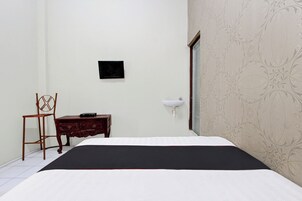 Un dormitorio con cama, una silla de madera, un aparador, un lavamanos en la pared y un papel tapiz estampado.