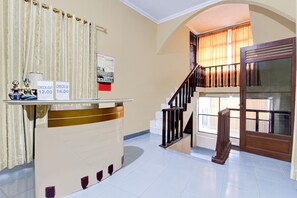 Un mostrador de recepción con letreros de salida y entrada, una escalera y vistas al exterior a través de una ventana.
