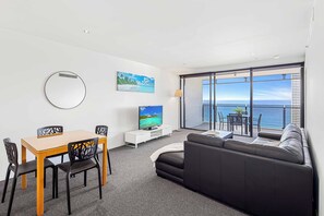 A modern living room with a dining area, a flat-screen TV, and a large window overlooking the sea. - Circle on Cavill Ocean View (Surfers Paradise)