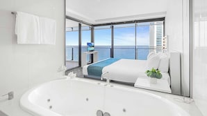 A modern hotel room with a large bathtub, a bed with a blue blanket, a small table with a plant, and a TV on a stand. - Circle on Cavill Ocean View (Surfers Paradise)