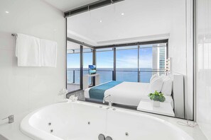 A modern hotel room with a large bathtub, a bed with a blue blanket, a small table with a plant, and a TV on a stand. - Circle on Cavill Ocean View (Surfers Paradise)