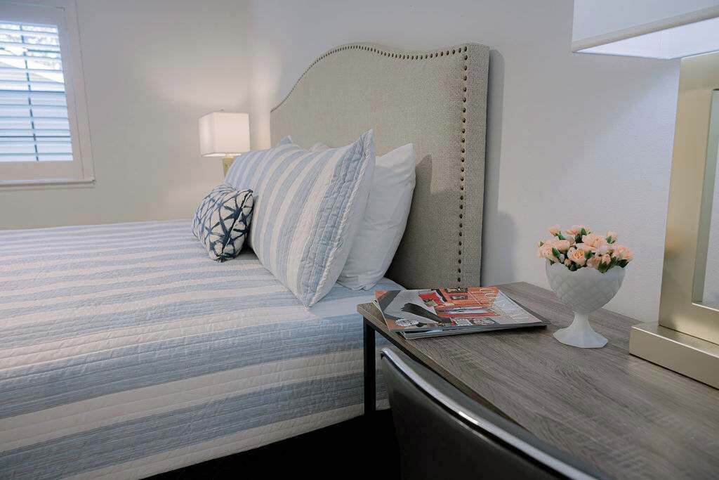 A neatly made bed with striped bedding, a bedside table with a lamp, and a vase with flowers.