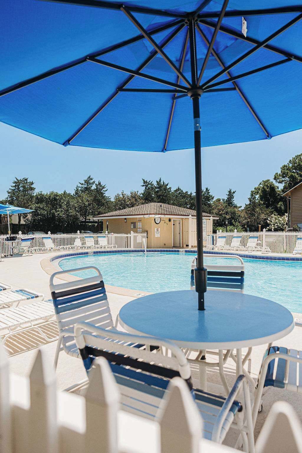 A poolside area with lounge chairs, a table, and a blue umbrella.