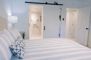 A bedroom with a bed, a nightstand, a lamp, and a door leading to a bathroom. - Villa Bandido-Golf Course, Pool, Tennis Court, Pet Friendly, & Golf Cart Deals (Miramar Beach)