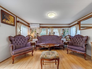 Ein Zimmer mit einem großen, gepolsterten Sofa, zwei Sesseln, einem Holztisch und einem blumengemusterten Ottomanen.