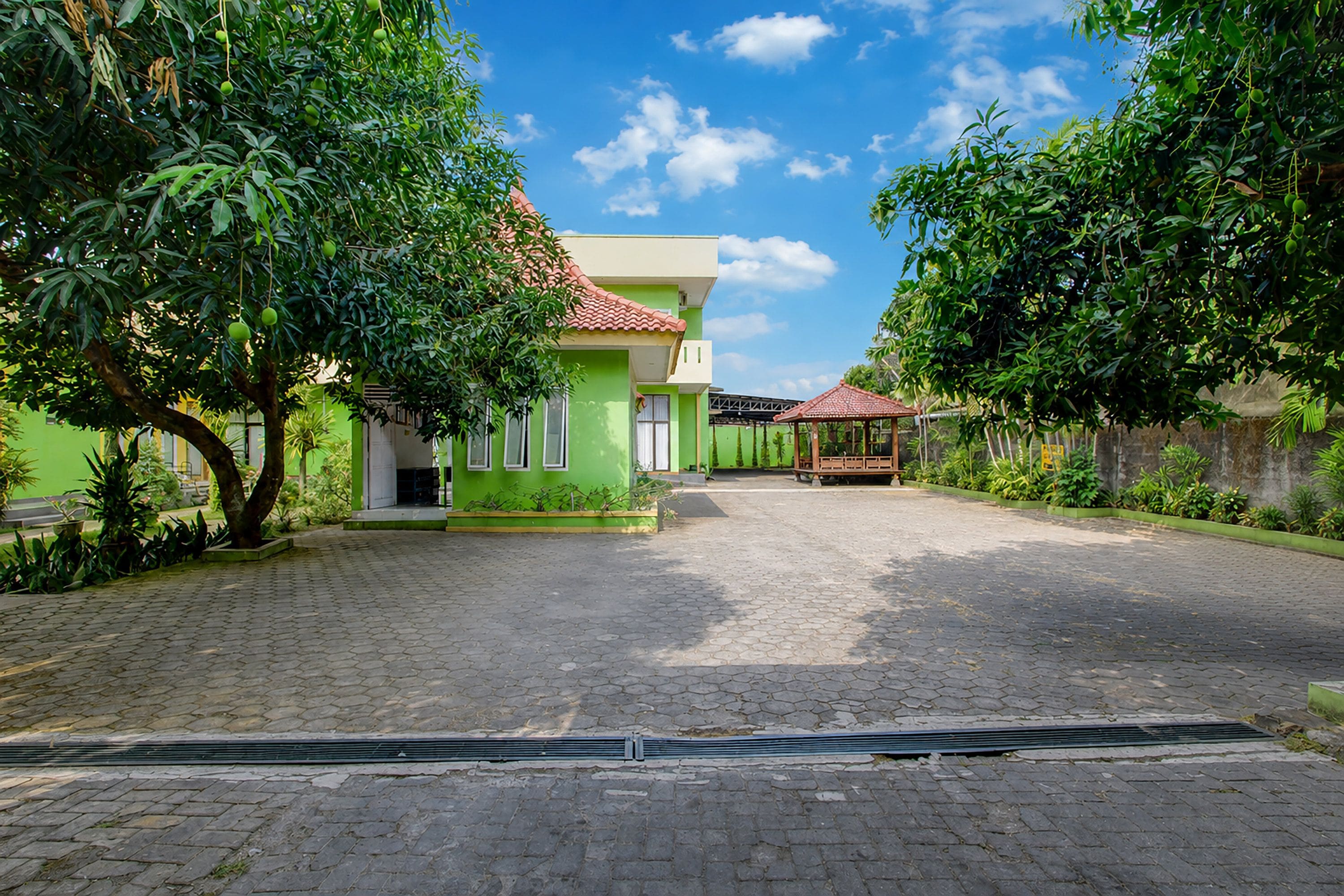 A courtyard with a green building, paved walkway, and a gazebo.