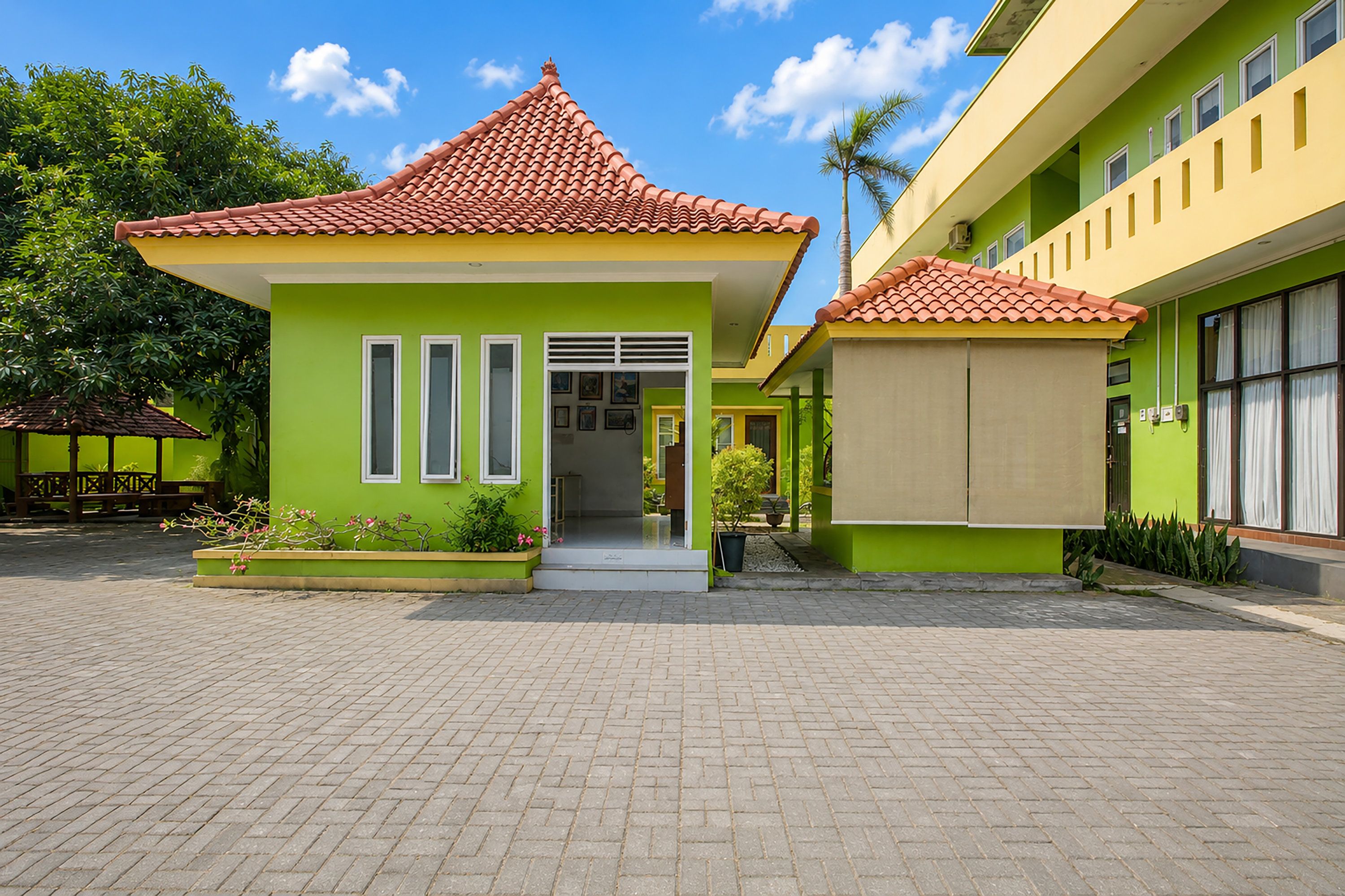 A building with a red-tiled roof, green walls, and a paved courtyard.