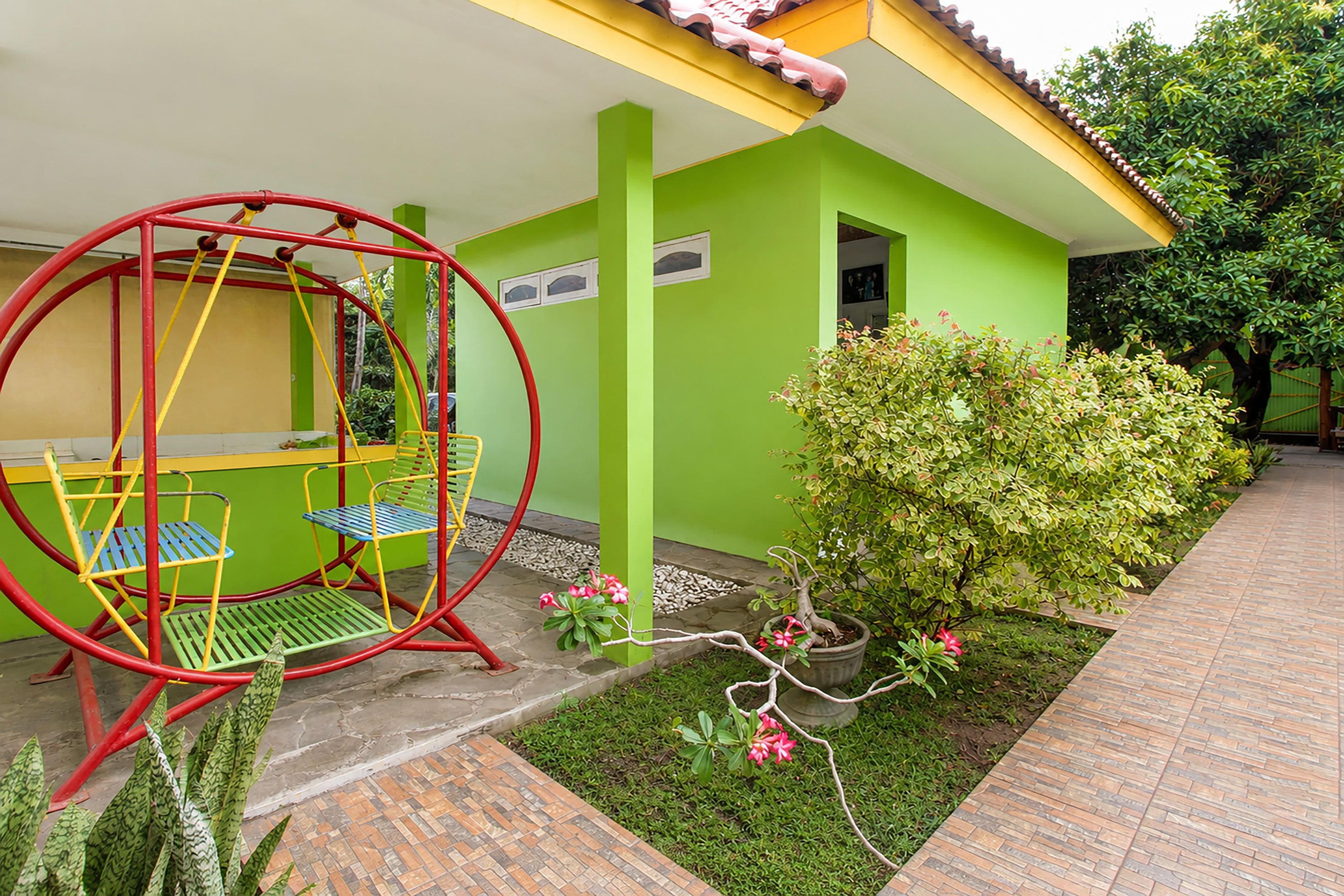 A green building with a swing set and a small garden with a potted plant and flowers.