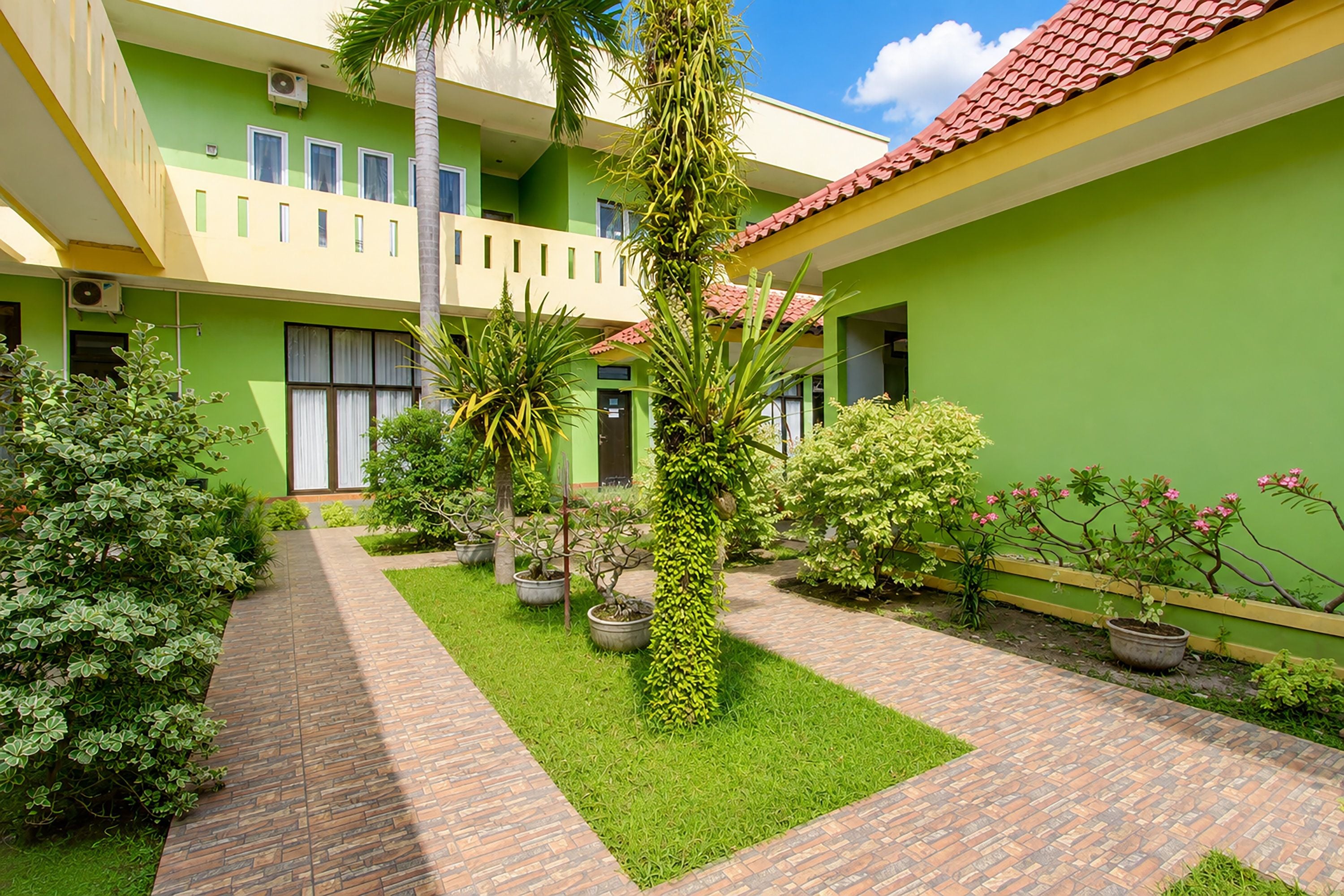 A courtyard with a brick pathway, green walls, and potted plants.