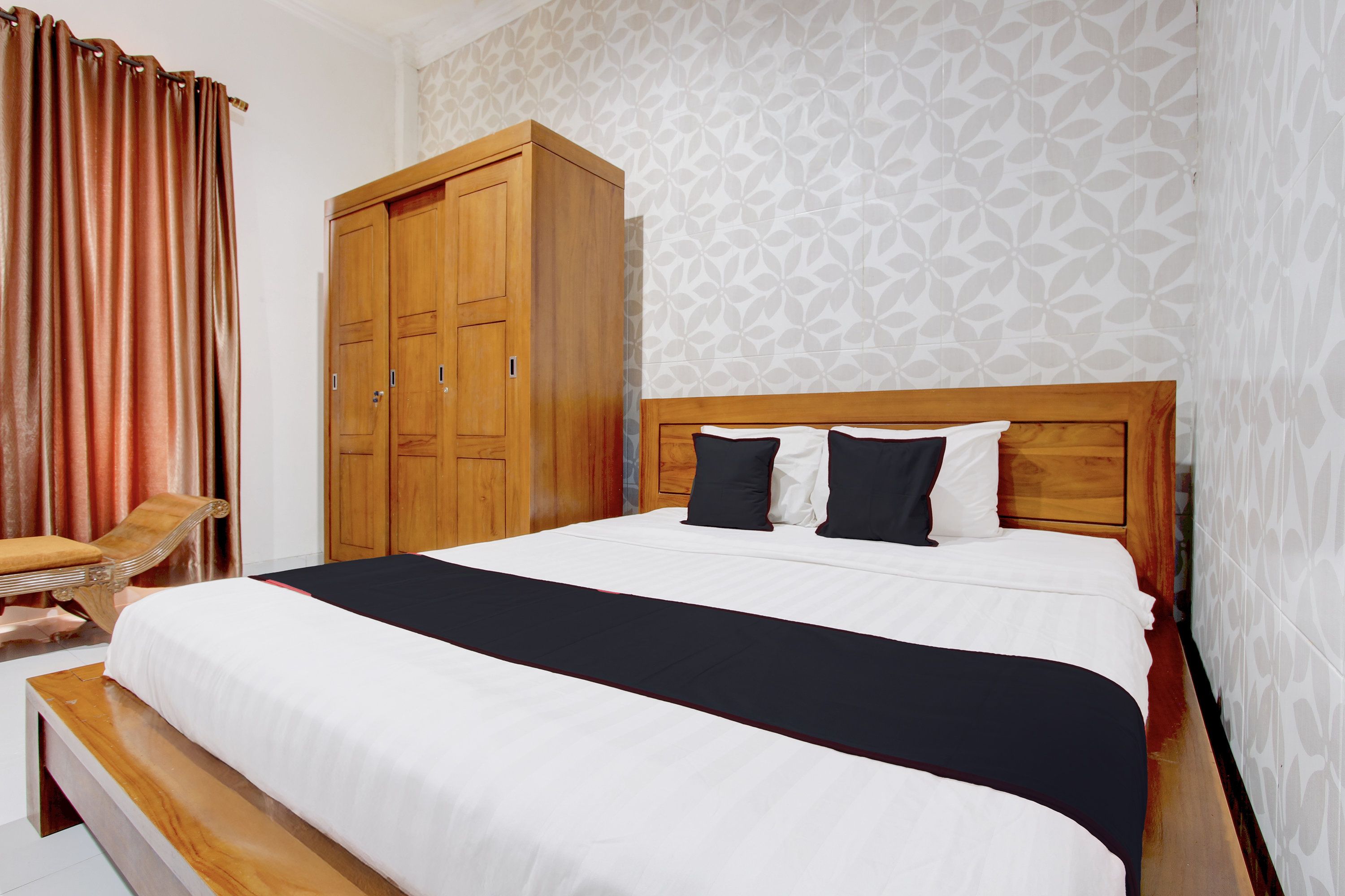 Una habitación de hotel con una cama, un armario de madera, una silla y un papel tapiz estampado.