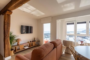 A modern living room with a large window, a flat-screen TV, and a cozy seating area. - Geure portue etxea, wonderful sunrise (Bermeo)