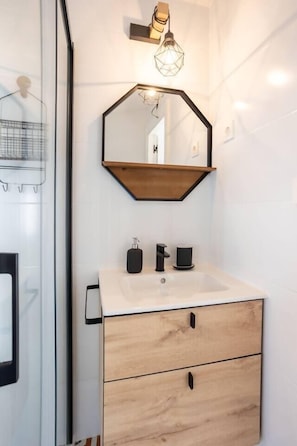 A bathroom with a white sink, wooden cabinet, and a mirror with a geometric light fixture above it. - Geure portue etxea, wonderful sunrise (Bermeo)