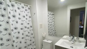 A bathroom with a toilet, sink, and shower curtain with eye patterns. - Apartment in Alicura - Pucón (Pucon)
