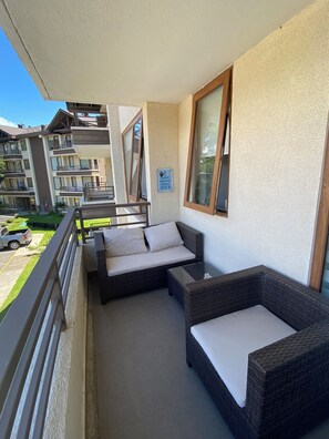 Ein Balkon mit Korbmöbeln, ein Schild zur Wassereinsparung und Blick auf ein mehrstöckiges Gebäude.