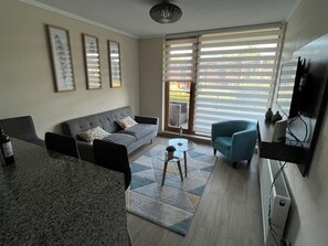 Ein Wohnzimmer mit einer Couch, einem Couchtisch und einem Fernseher. An der Wand hängen drei gerahmte Bilder.