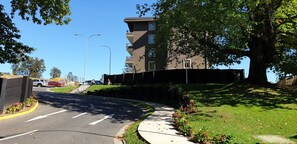 Eine Wohnstraße mit Fußweg, parkenden Autos und einem mehrstöckigen Gebäude mit Balkonen.