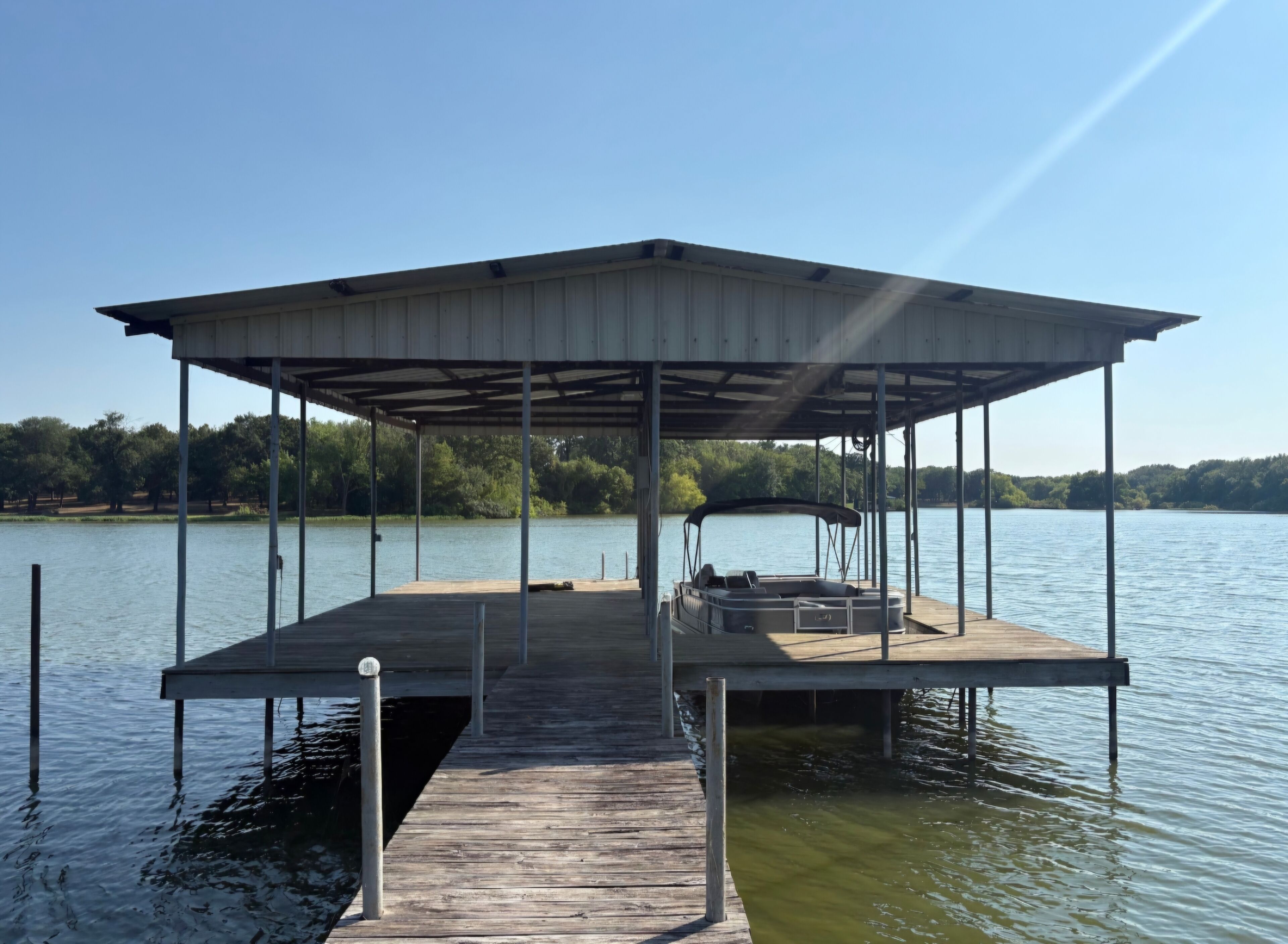 Un muelle techado con un barco, rodeado de agua tranquila y árboles.