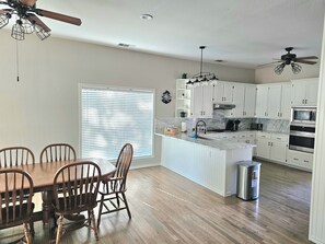 A kitchen with white cabinets, a central island, and a dining area with wooden chairs. - Waterfront LakeHouse with dock in peaceful Quinlan with option of boat rental. (Quinlan)