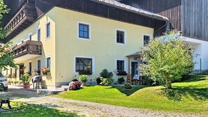 Ein zweistöckiges Gebäude mit einem Balkon und einem Garten mit verschiedenen Pflanzen, bewölkter Himmel.