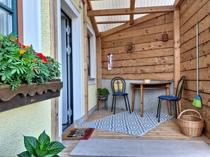 A wooden exterior porch with a table and chairs, a hanging plant, and a door.