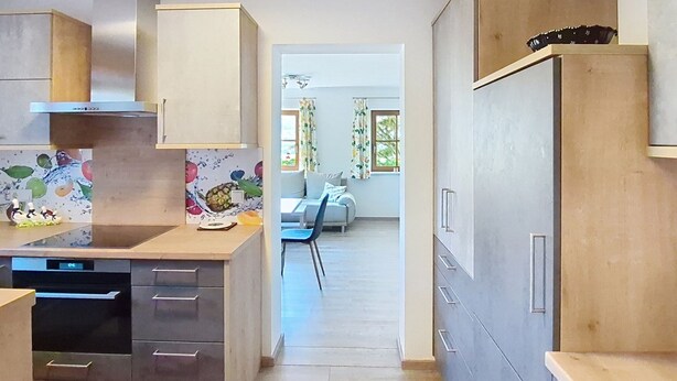 Eine moderne Küche mit Einbaugeschirrspüler, ein Essbereich mit Tisch und Stühlen sowie Blick in das Wohnzimmer durch einen offenen Durchgang.