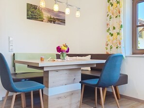 A dining area with a table, chairs, a vase of flowers, and a painting on the wall.