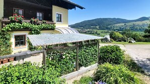 Ein zweistöckiges Haus mit Balkon, umgeben von üppiger Vegetation und Blick auf sanfte Hügel.