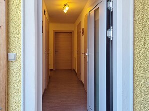 A narrow hallway with wooden flooring, doors on both sides, and a light fixture on the ceiling.