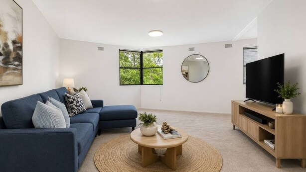 Uma sala de estar moderna com um sofá modular, uma mesa de centro, uma televisão e uma janela ampla.