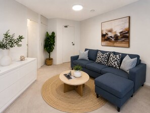 A modern living room with a blue sofa, a round coffee table, a white cabinet, and a large abstract painting on the wall. - Trendy Studio Apartment With Harbour Bridge Views (Sydney)