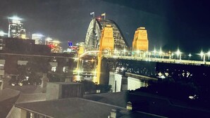 Vista noturna de uma ponte com duas torres imponentes e uma via iluminada.
