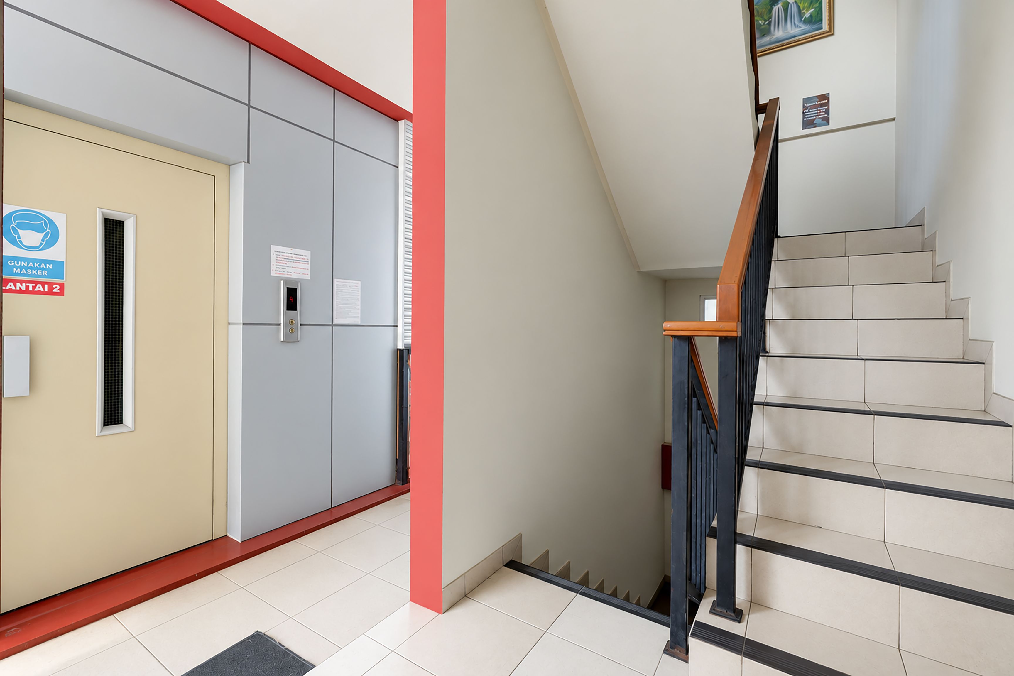 A hotel entrance with a staircase, a sign indicating a mask requirement, and a door with a digital display.
