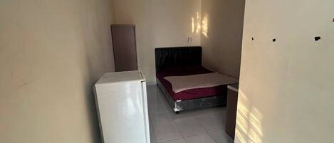 A small, narrow room with a bed, a wardrobe, and a refrigerator.