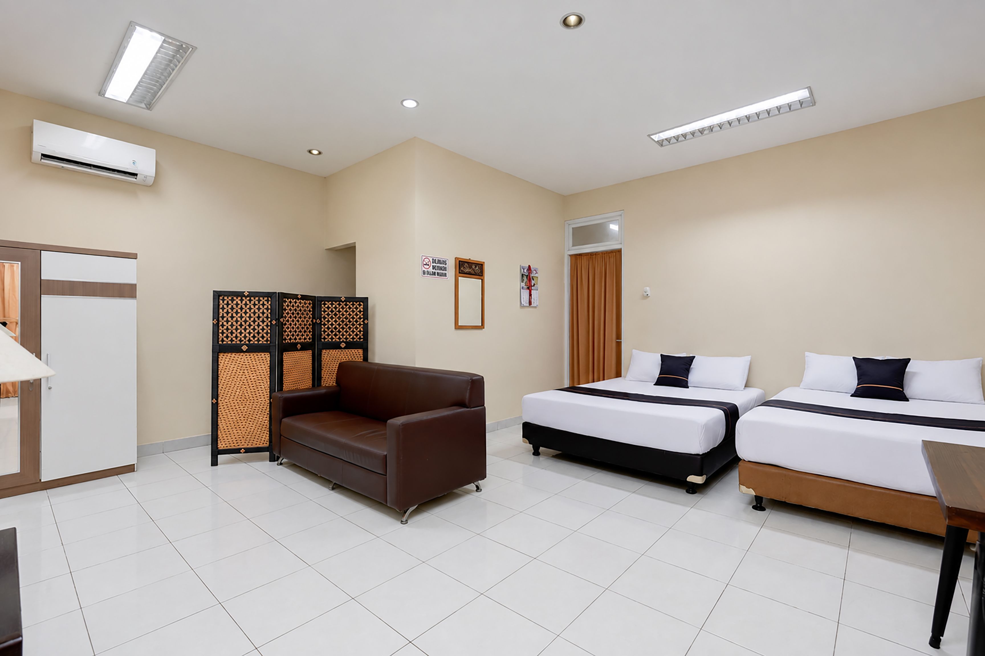 A hotel room with a sofa, two single beds, a desk, and a partition.