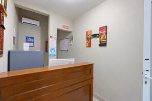 A reception area with a wooden desk, a whiteboard, and a wall-mounted air conditioner. - Collection O near Taman Semanggi (Jakarta)